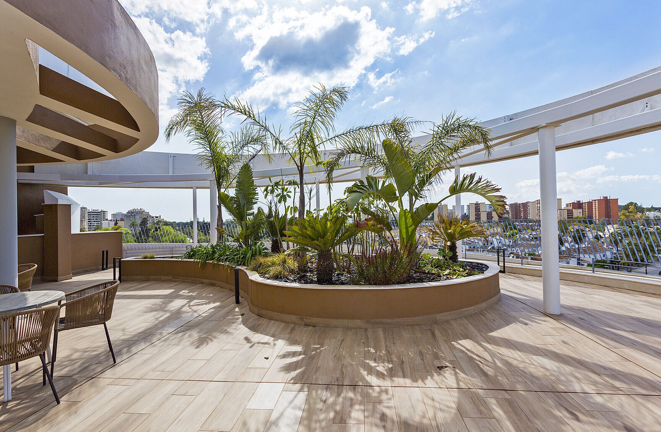 An outdoor patio with a curved seating area, a planter with tropical plants, and a view of the cityscape.