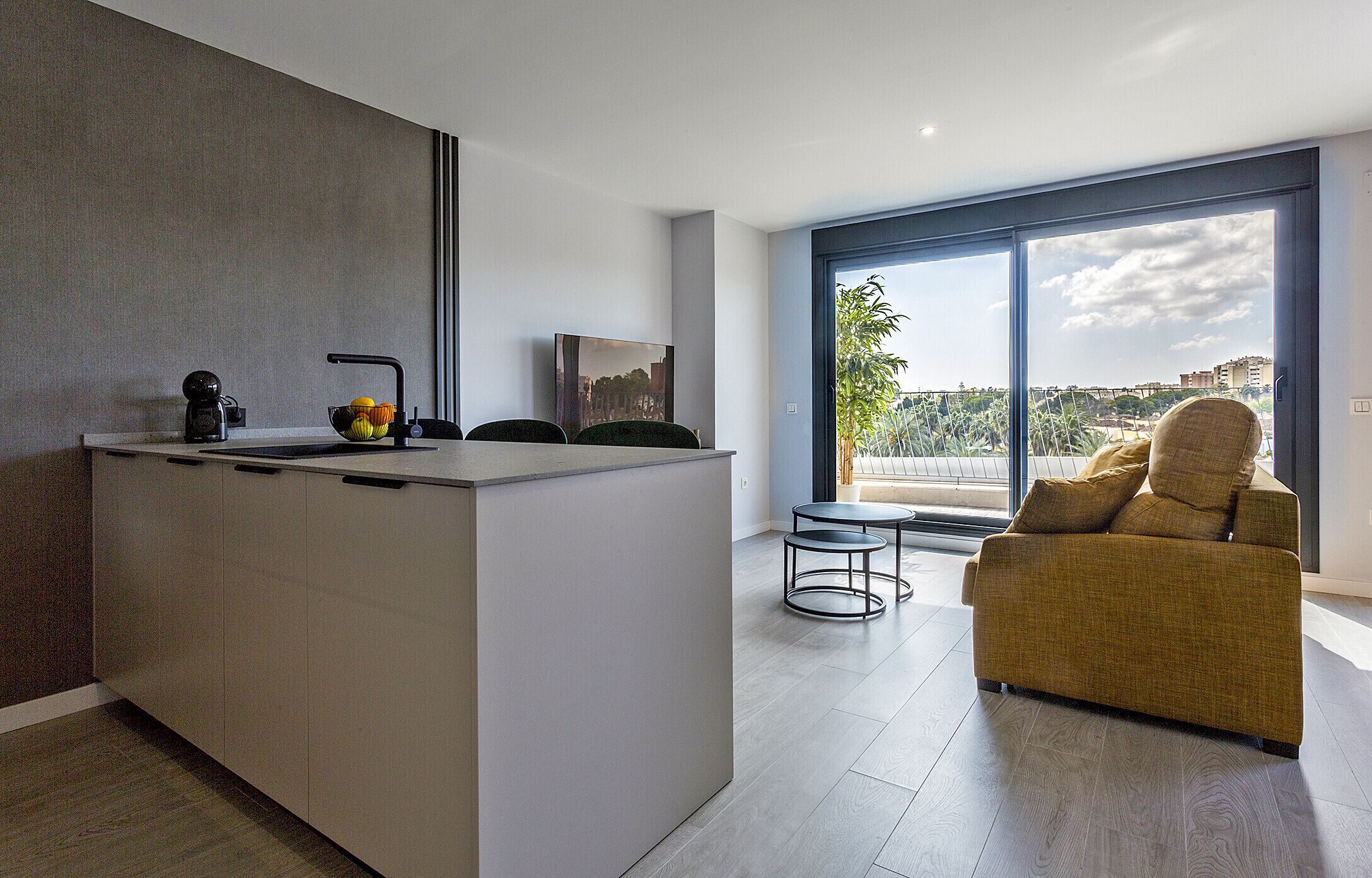 Eine moderne Küche mit einer zentralen Kochinsel, ein Essbereich mit einer Couch und ein großes Fenster mit Blick auf die Stadt.