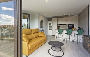A modern living area with a sofa, a round table, and a kitchen in the background. - Sky Garden Jerez - Ole Solutions (Jerez de la Frontera)