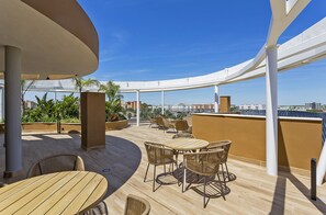Eine Terrasse im Freien mit einem runden Tisch und Korbstühlen, umgeben von einer weißen Pergola.