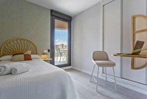 A modern hotel room with a large bed, a desk with a laptop, and a view of the city through a glass door. - Sky Garden Jerez - Ole Solutions (Jerez de la Frontera)