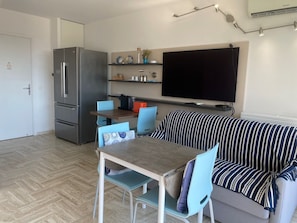 Ein kompakter Wohnbereich mit Küchenzeile, Essbereich und einer Sitzecke mit Sofa und Wandfernseher.
