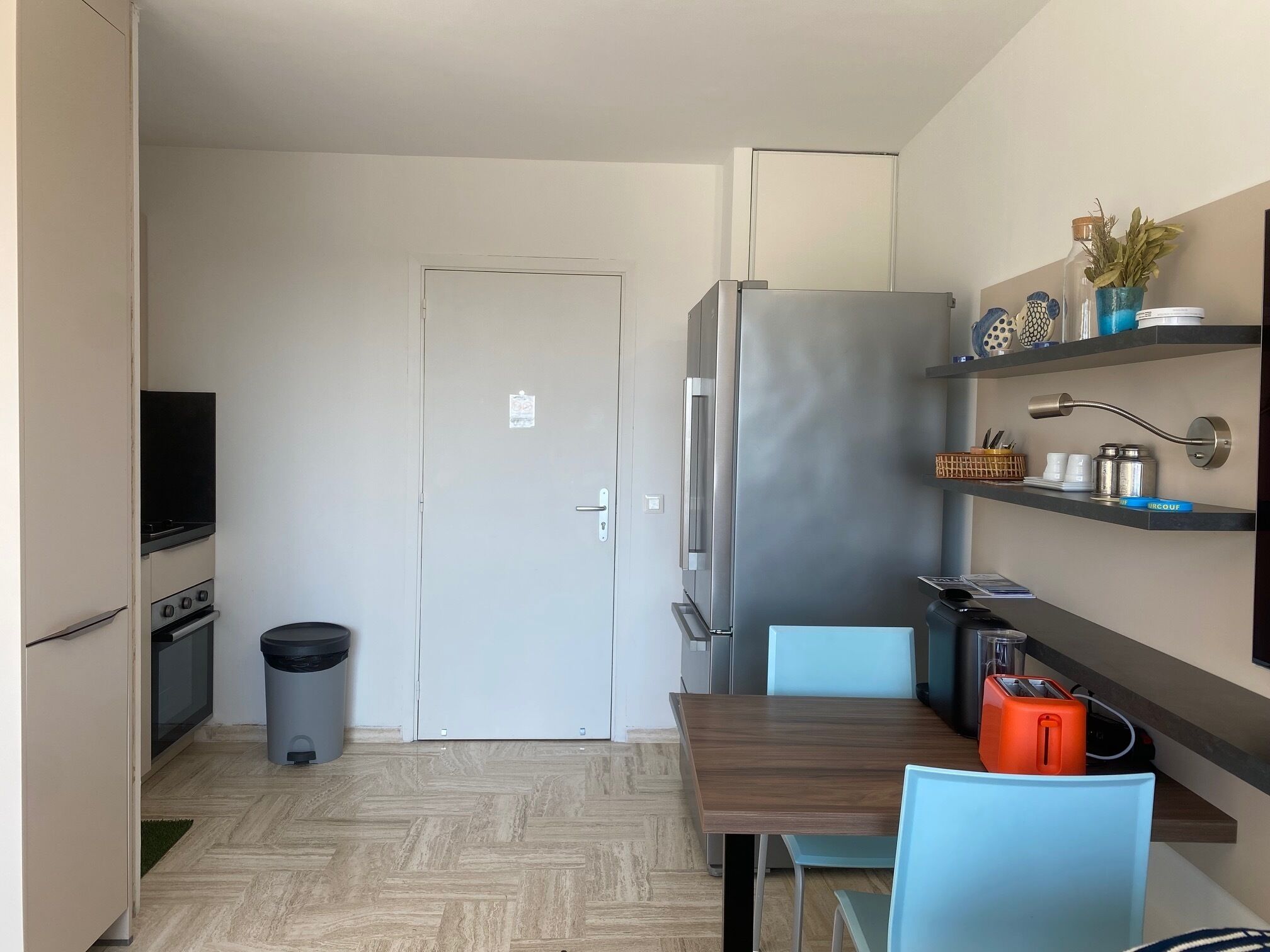 A compact kitchen with a refrigerator, stove, and trash bin.