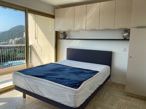 A modern bedroom with a bed, a view of a swimming pool, and a balcony. - Large Studio in Canne Marina (Mandelieu-la-Napoule)