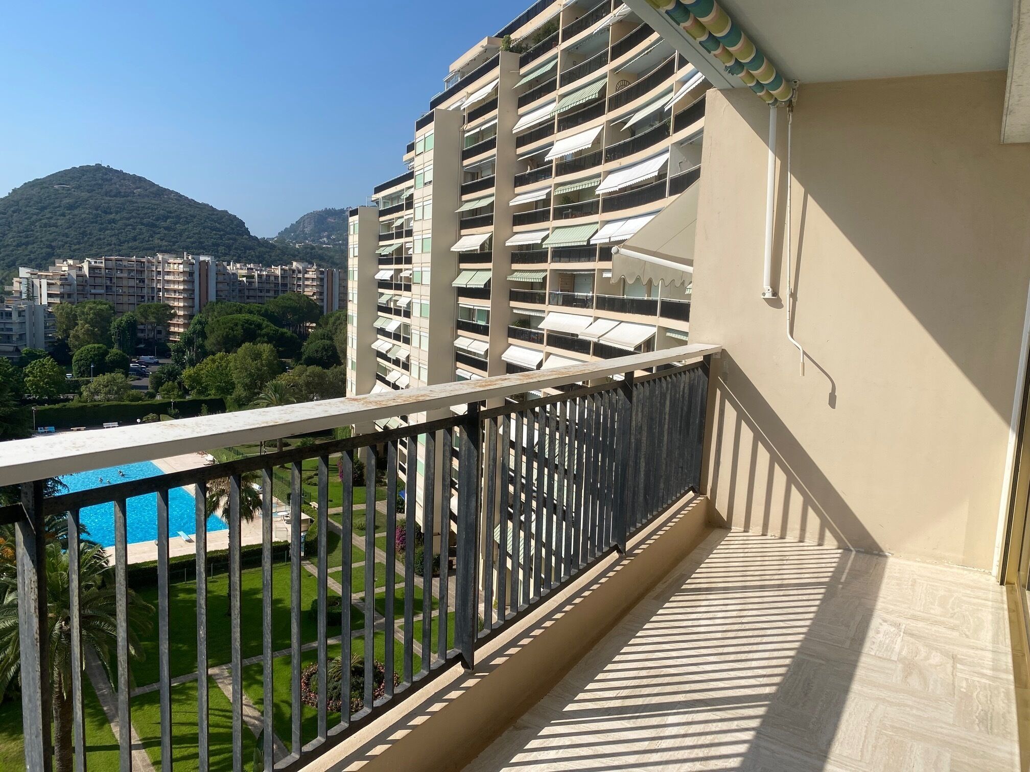 Uma varanda com vista para uma piscina, uma montanha e edifícios ao redor.