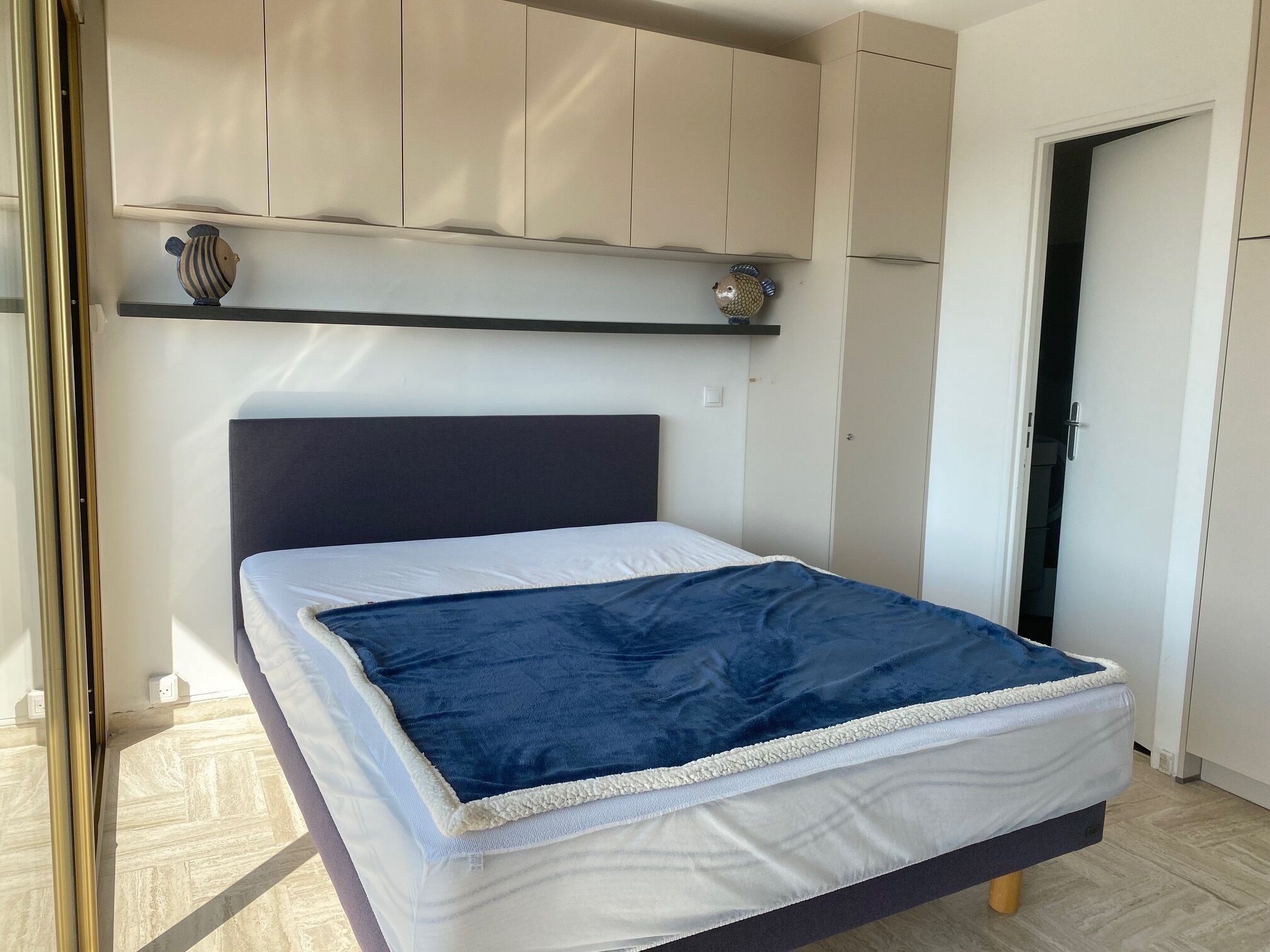 A bedroom with a bed, a headboard, a shelf with decorative items, and a door.