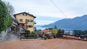 Ein zweistöckiges Gebäude mit einem Balkon, einem Feldweg und Blick auf Berge und einen See.