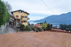 Ein zweistöckiges Gebäude mit einem Balkon, einem Feldweg und Blick auf Berge und einen See.