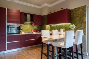Een moderne keuken met rode kastjes, een roestvrijstalen fornuis en een groene betegelde achterwand.