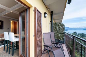 Een balkon met een tafel en stoelen, uitzicht op zee en een berg op de achtergrond.