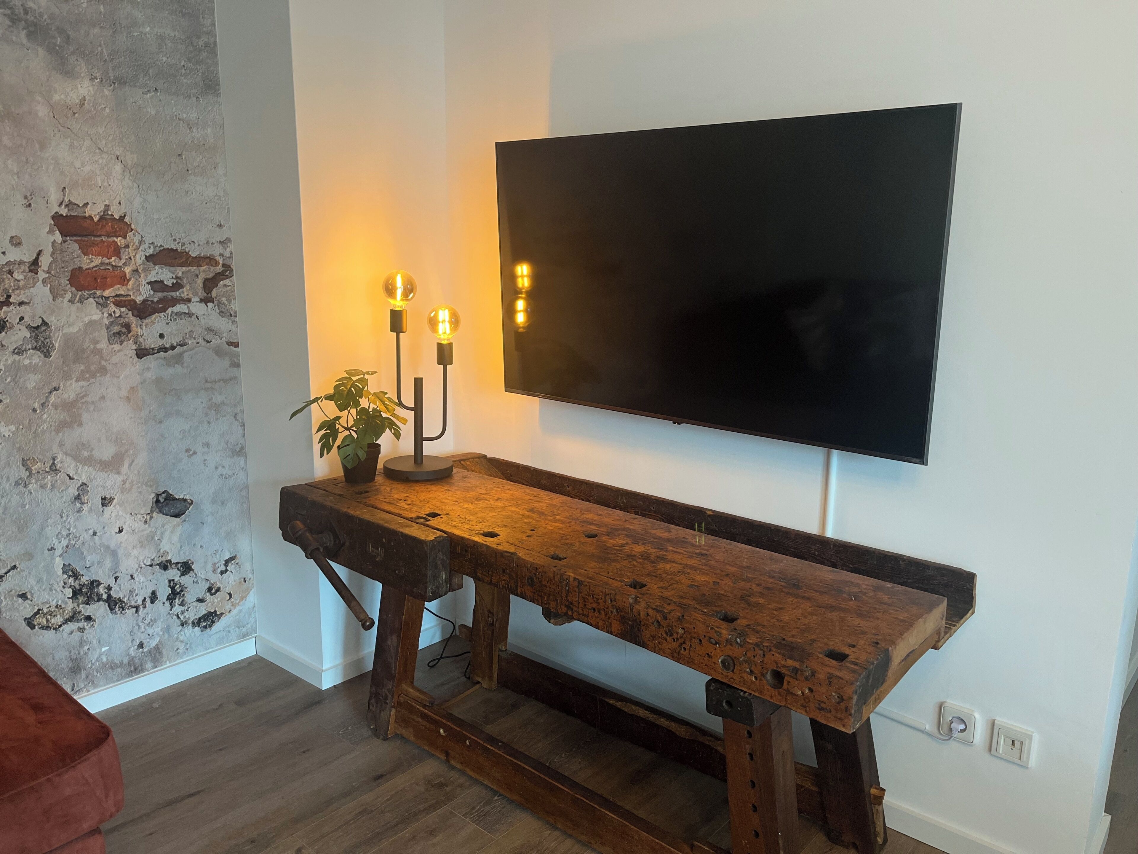 Ein Zimmer mit einer hölzernen Sitzbank, einem Blumentopf und einem flachbildfernseher an der Wand.