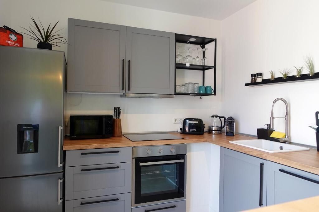 Eine moderne Küche mit grauen Schränken, einem Edelstahl-Kühlschrank, einer Mikrowelle, einem Toaster und einem Spülbecken.
