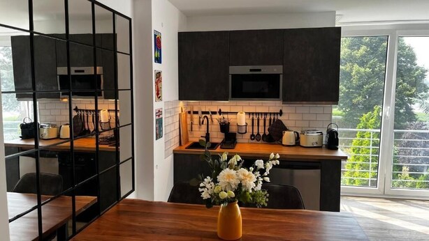 Eine moderne Küche mit dunklen Schränken, einer Holzausziehtafel und einem Essbereich mit einem Blumenstrauß.