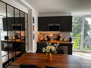 A modern kitchen with dark cabinets, a wooden countertop, and a dining area with a vase of flowers. - Chrisma Apartments (Düsseldorf)