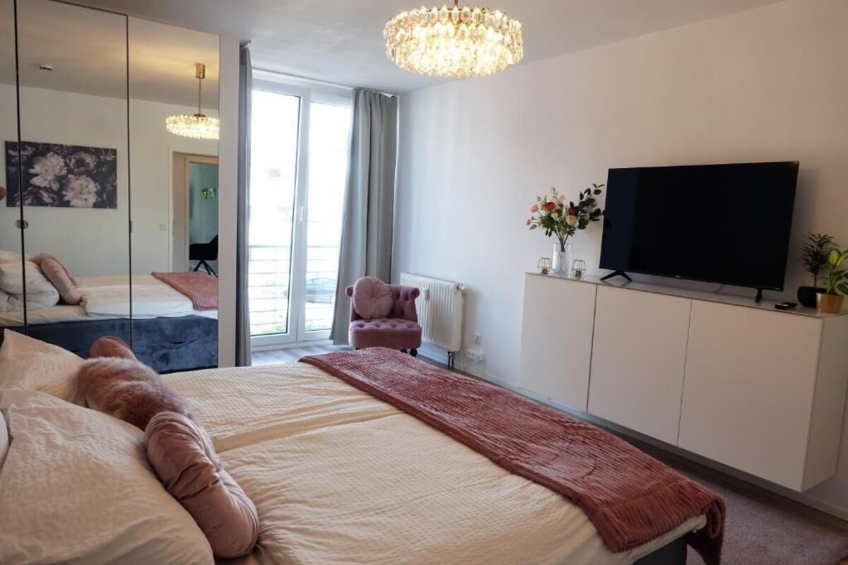 Ein Hotelzimmer mit einem Bett, einem Fernseher, einem Sessel, einem Spiegel und Blick ins Freie.