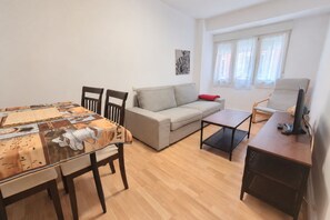 A living room with a dining table, two chairs, a sofa, a small table, and a TV stand. - 1A174 Central Apartment in Gijón (Gijón)
