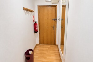 A hallway with a wooden door, a fire extinguisher mounted on the wall, and a trash bin. - 1A174 Central Apartment in Gijón (Gijón)