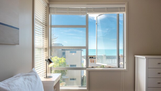 Ein Schlafzimmer mit einem Bett, einem Schreibtisch mit Lampe, einer Kommode und einem Fenster mit Jalousien.