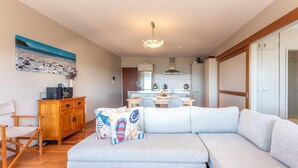 Ein modernes Wohnzimmer mit grauem Sofa, Holzschrank und einem Gemälde von einer Strandansicht.