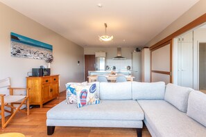 Ein modernes Wohnzimmer mit grauem Sofa, Holzschrank und einem Gemälde von einer Strandansicht.