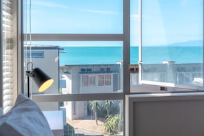 Ein Zimmer mit großem Fenster und Blick auf die Küste, einer Lampe und einem Bett.