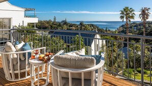 Ein Balkon mit Gartenmöbeln, einem Tisch mit Flasche und Glas sowie einem herrlichen Blick auf das Meer und die Hügel.