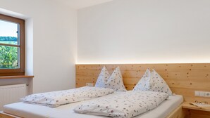 Una cama doble con ropa de cama floral, un cabecero de madera, una mesita de noche con vasos y una ventana con vistas al verdor.