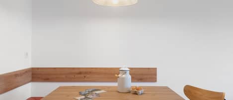 Une table en bois avec un pichet blanc et des œufs, une chaise en bois et un luminaire suspendu.