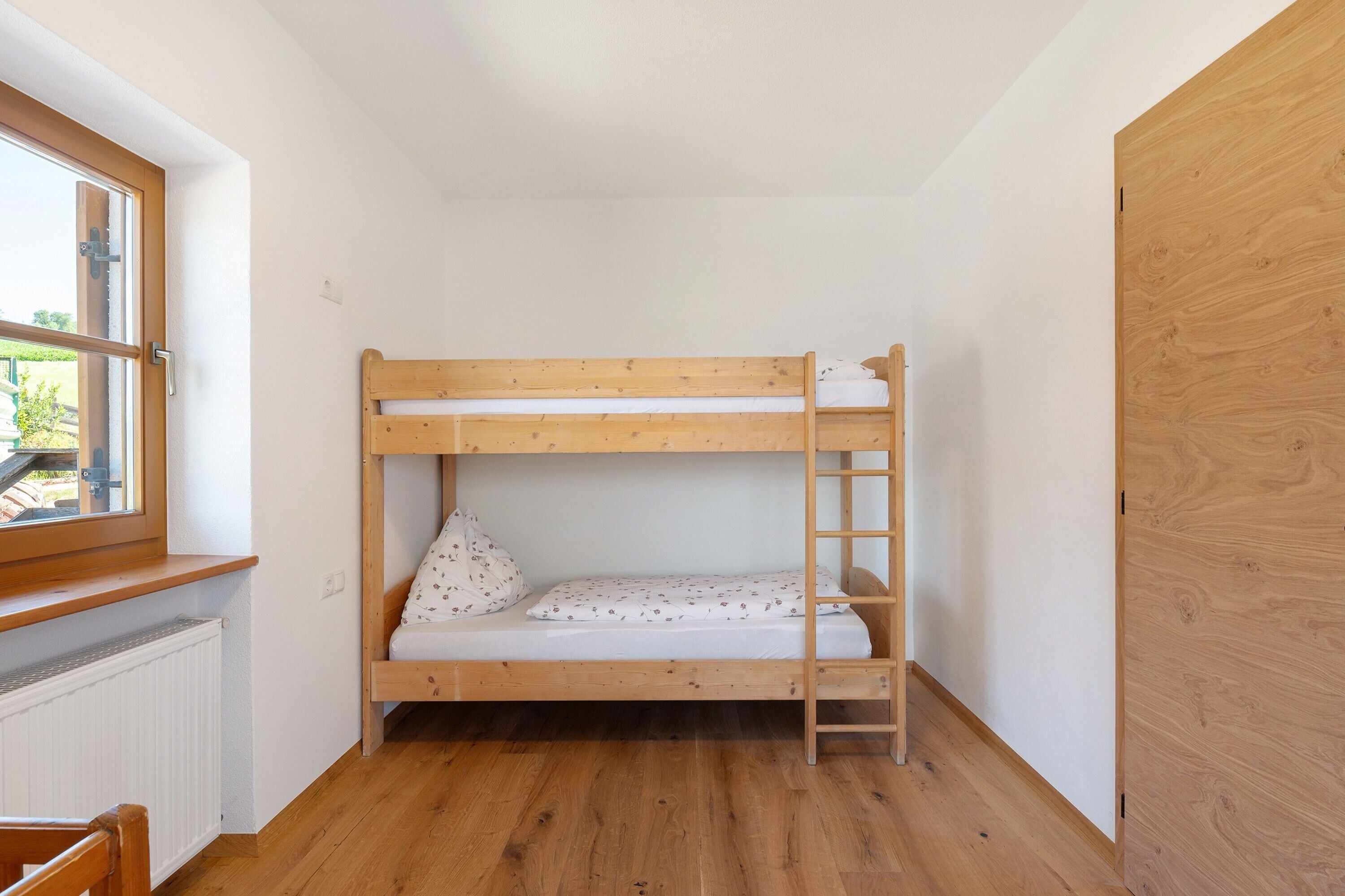 Un lit superposé avec une échelle, une fenêtre donnant sur un beau paysage et un radiateur.