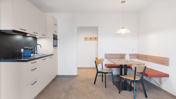 Cocina moderna con comedor, que incluye un horno empotrado, una cafetera y una lámpara colgante.