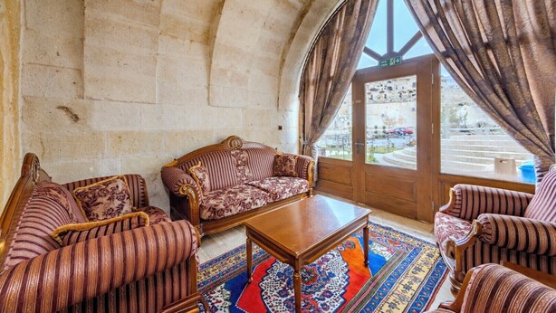 Une pièce avec un mur en pierre, une porte en bois, un canapé à motifs, une table basse en bois et des fauteuils à rayures.