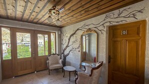 Una habitació amb sostre de fusta, un mirall gran, dues cadires antigues, una taula petita i una porta amb placa de número.
