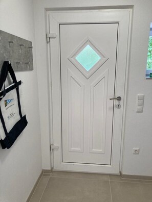 A white door with a diamond-shaped window, a wall-mounted plaque, and a tiled floor.