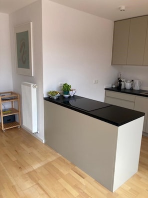Une cuisine moderne avec un plan de travail noir, des placards blancs, un radiateur et une petite étagère en bois.