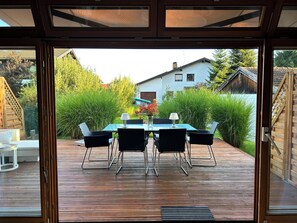 An outdoor deck with a table and chairs, a wooden fence, and a view of a house and greenery. - Vrbo Property (Gstadt am Chiemsee)