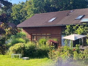 A modern house with a sloped roof, large windows, and a garden with various plants and a table.
