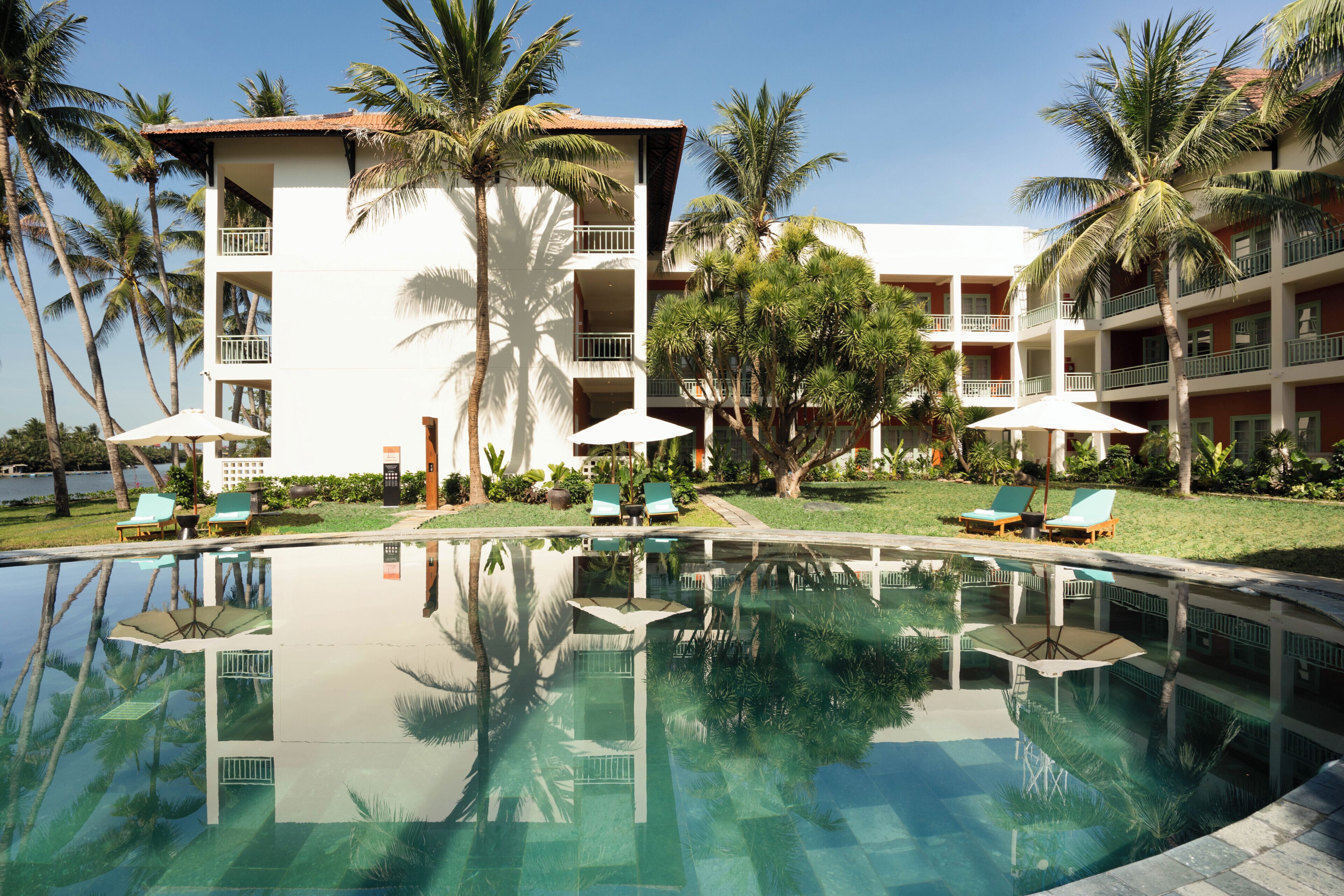 A hotel with a swimming pool, palm trees, and lounge chairs.
