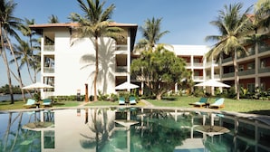 A hotel with a swimming pool, palm trees, and lounge chairs. - M Village Resort Riverbeach Hoi An (Da Nang)