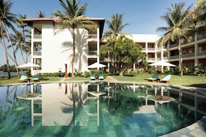 A hotel with a swimming pool, palm trees, and lounge chairs.