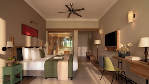 A hotel room with a bed, bedside table, desk, chair, and a ceiling fan. - M Village Resort Riverbeach Hoi An (Da Nang)