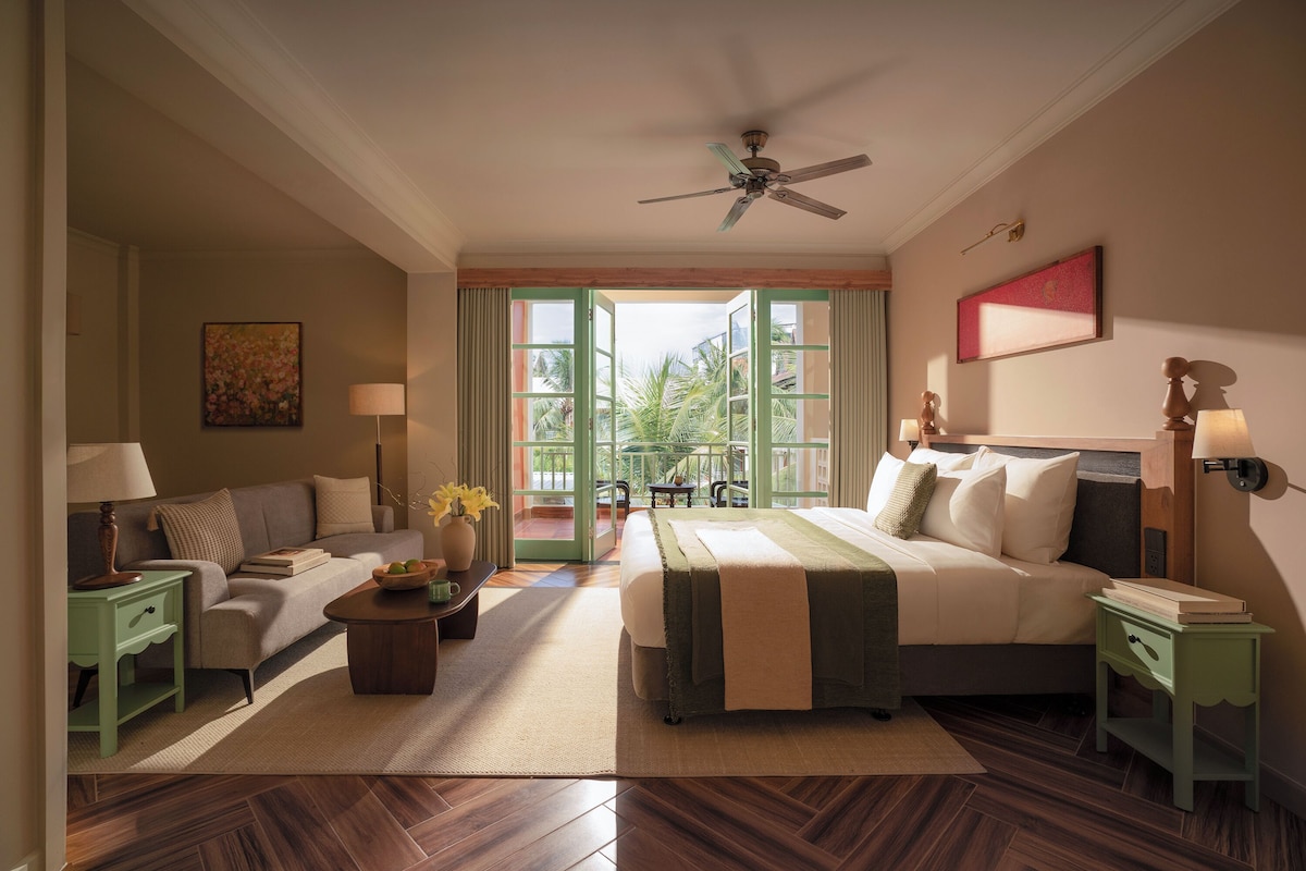 A hotel room with a bed, a sofa, a coffee table, and a view of the outdoors.