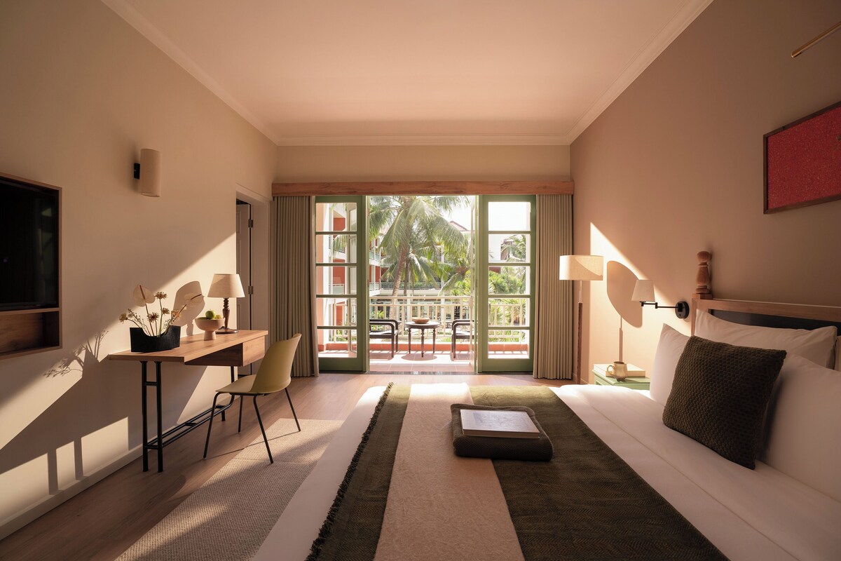 A hotel room with a bed, a desk with a chair, a television, and a view of the outdoors.