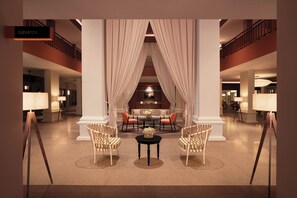 A lobby with a central seating area, a staircase, and a sign indicating an elevator. - M Village Resort Riverbeach Hoi An (Da Nang)