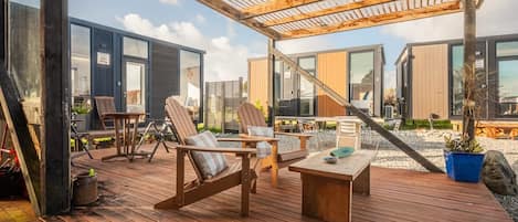 A wooden deck with outdoor seating, including chairs and a table, overlooking a modern building with large windows.