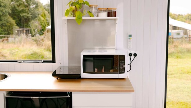 A compact kitchen with a microwave, a shelf with jars, and a potted plant. - Rimu View 6 by Tiny Away (Ruatapu)