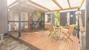 A covered outdoor area with wooden flooring, seating, and a sheltered entrance. - Rimu View 6 by Tiny Away (Ruatapu)