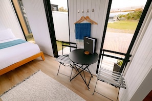 Ein Schlafzimmer mit einem Bett, einem kleinen Tisch und einem Stuhl. Ein Fenster bietet Blick ins Freie.