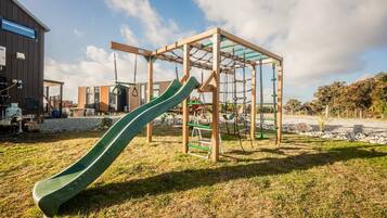 Ein Spielplatz mit Rutsche und Klettergerüsten, vor einer Bebauung und Bäumen.
