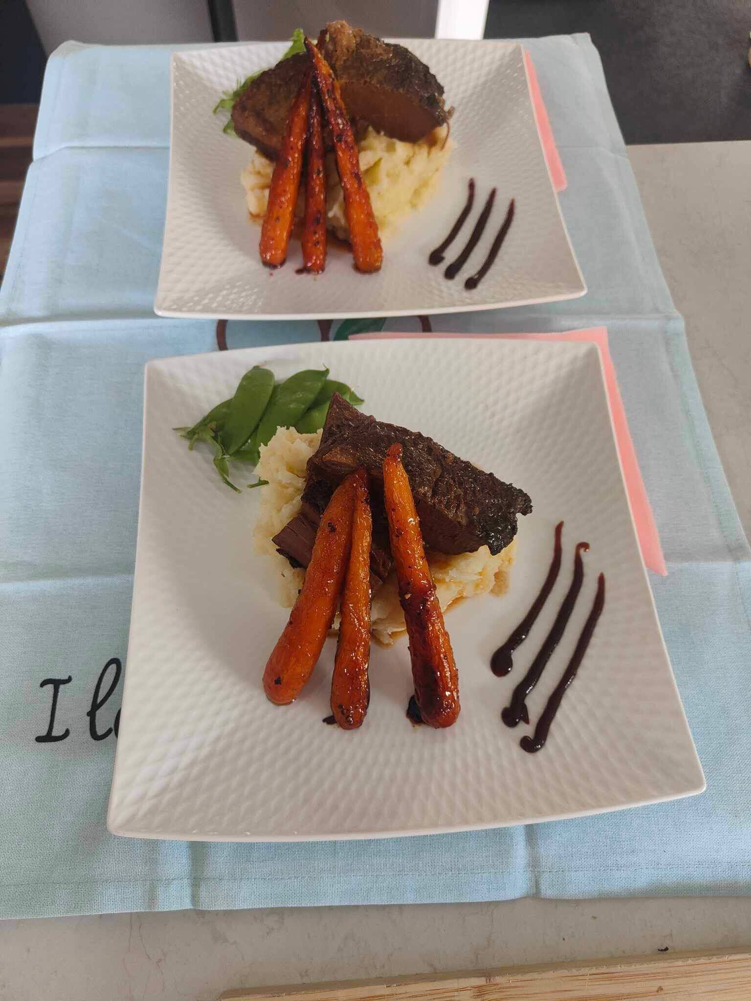 Dos platos cuadrados de comida con zanahorias y un guiso de carne oscura, sobre una mesa con mantel azul claro.