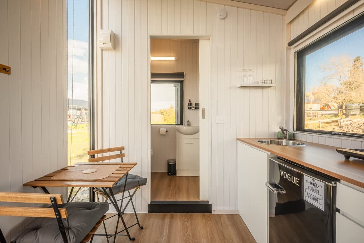 A compact kitchen with a wooden table and chairs, a sink, and a window with a view of the outdoors.